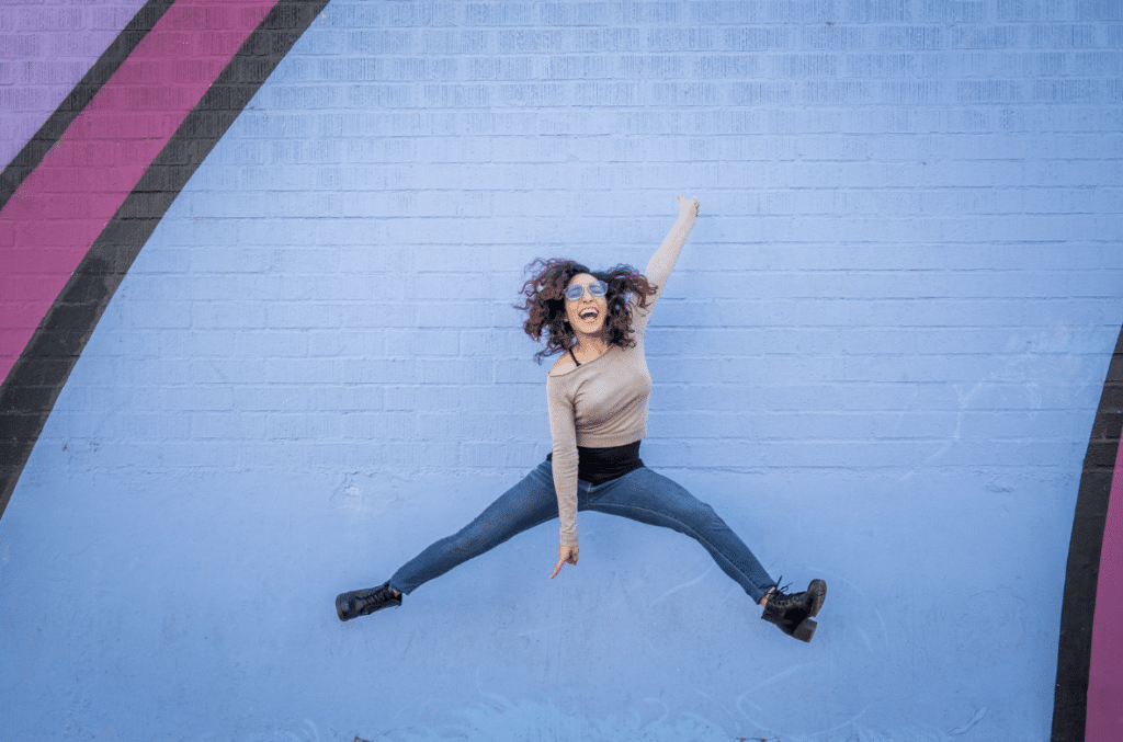 young hispanic woman jumping in front of a mural with a positive attitude